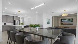 A modern kitchen with grey cabinets, a stainless steel refrigerator, and a dining area with a glass table and grey chairs. - Magic & Adventure in This Stunning home in CG (Davenport)