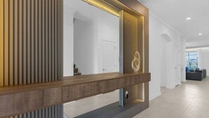 A modern reception area with a wooden reception desk, a large mirror, and a decorative wall panel. - Magic & Adventure in This Stunning home in CG (Davenport)