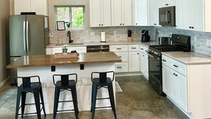 A modern kitchen with white cabinets, a central island with stools, stainless steel appliances, and a wooden ceiling. - Sunrise Chalet on Potato Lake - Water Front - Dock - Game Room - Hot Tub (Rusk Township)
