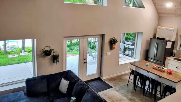 A modern interior with a kitchen, dining area, and a large window overlooking a green landscape. - Sunrise Chalet on Potato Lake - Water Front - Dock - Game Room - Hot Tub (Rusk Township)