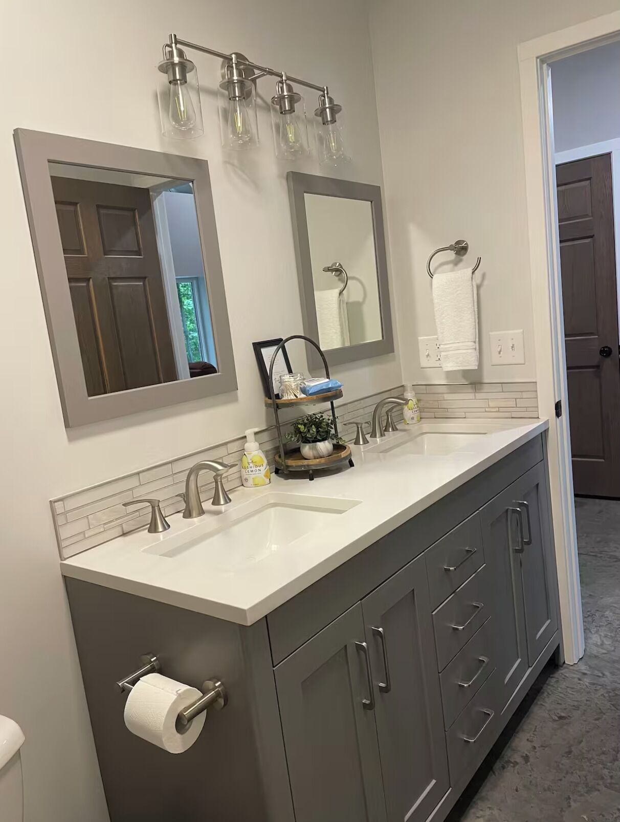 A modern bathroom with a double sink vanity, two wall-mounted mirrors, a towel rack, and a small plant on the vanity.