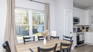 Eine moderne Küche mit weißen Schränken, einem Holztisch und Blick auf eine Wohngegend.