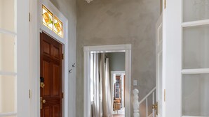 Un pasillo con piso a cuadros, una puerta de madera y una escalera con barandilla blanca.