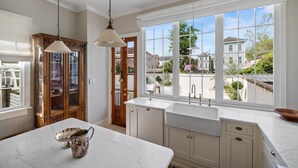 Una cocina con armarios blancos, encimera de mármol y un ventanal con vistas al barrio.