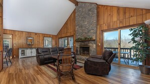 Un salón espacioso con pisos de madera, una chimenea de piedra y un amplio ventanal corredizo que da a un patio exterior.