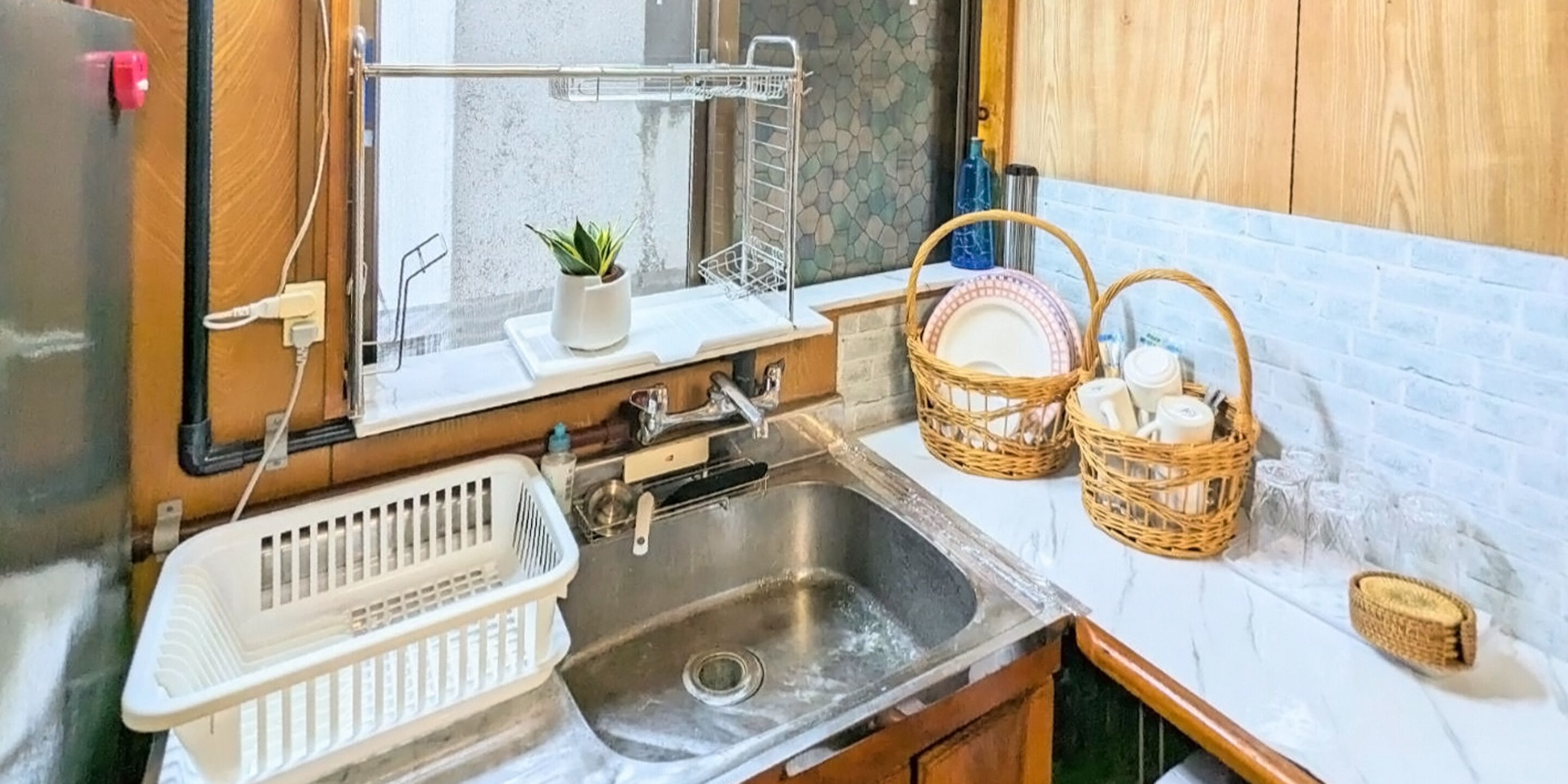 A kitchen with a stainless steel sink, a white countertop, a small potted plant, and wicker baskets.