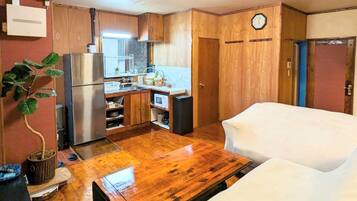 A compact kitchen with wooden cabinets, a refrigerator, a microwave, and a sink. There is a clock on the wall and a door to the right.