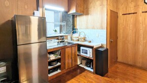 Una cucina compatta con mobili in legno, un frigorifero in acciaio inox, un forno a microonde e un piccolo elettrodomestico nero, probabilmente una macchina per il caffè.