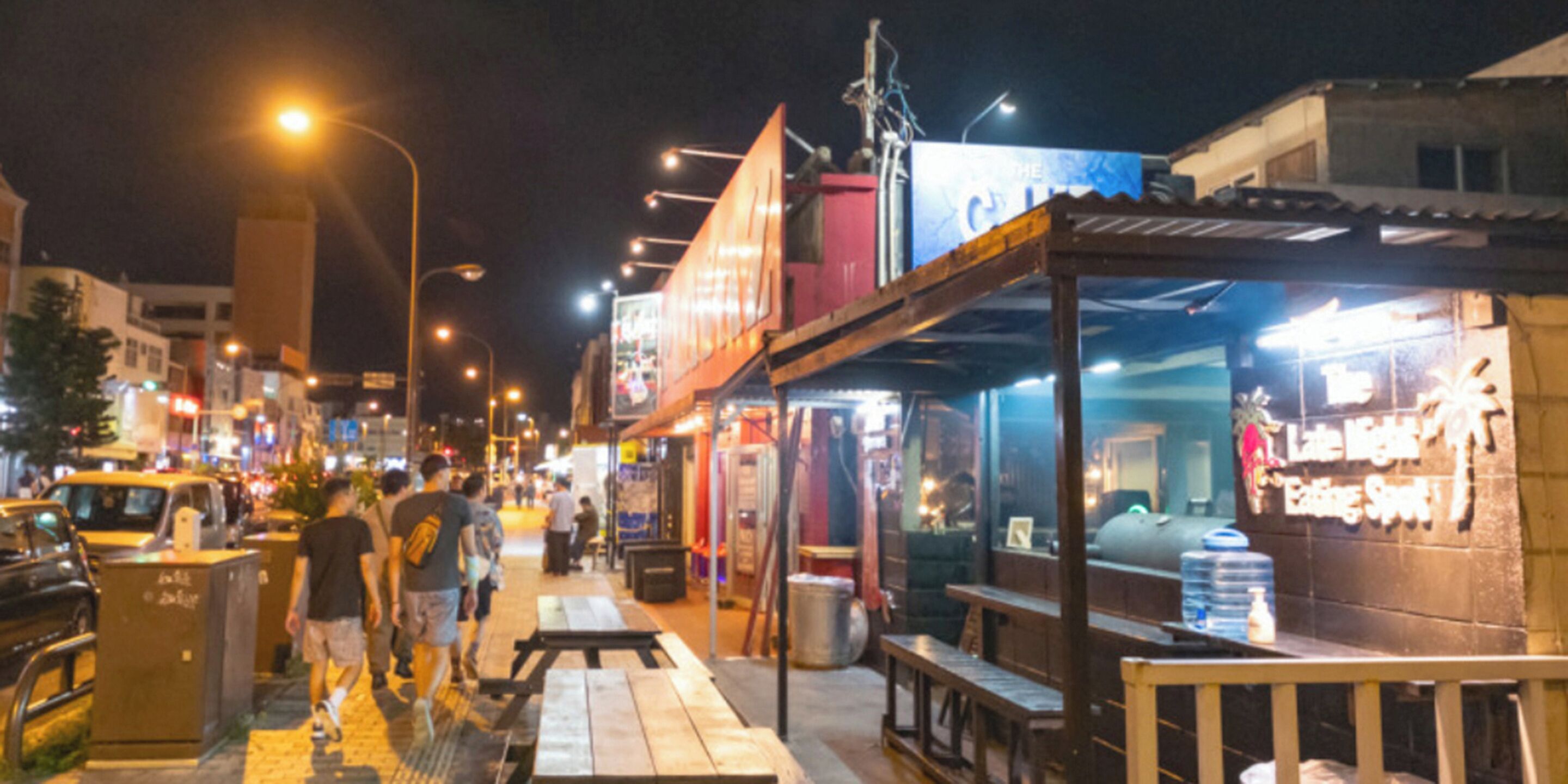A nighttime street scene with outdoor seating and illuminated signs.