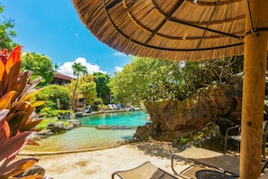 A pool area with lounge chairs, a thatched umbrella, and a rocky backdrop.