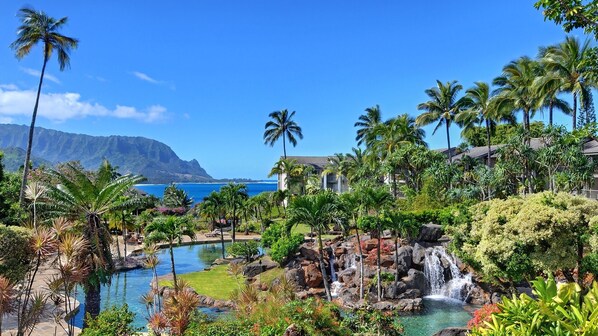 A tropical resort with a pool, waterfall, and ocean view.