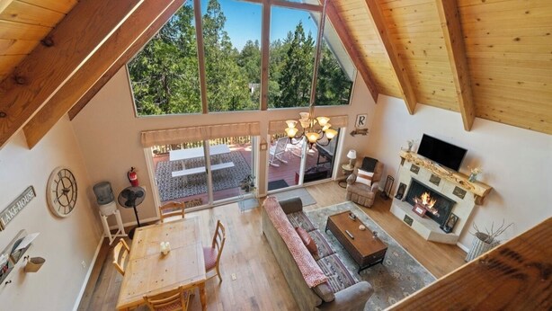 A spacious loft with a large skylight, a cozy fireplace, and a dining area. - Views! Sunsets! Amenities! A-Frame Cabin Sleeping 8 Guests. Come Relax & Unwind! (Lake Arrowhead)