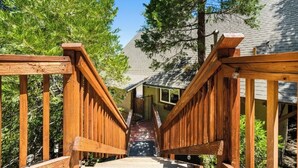 A wooden staircase leading to a building with a sloped roof, surrounded by trees. - Views! Sunsets! Amenities! A-Frame Cabin Sleeping 8 Guests. Come Relax & Unwind! (Lake Arrowhead)
