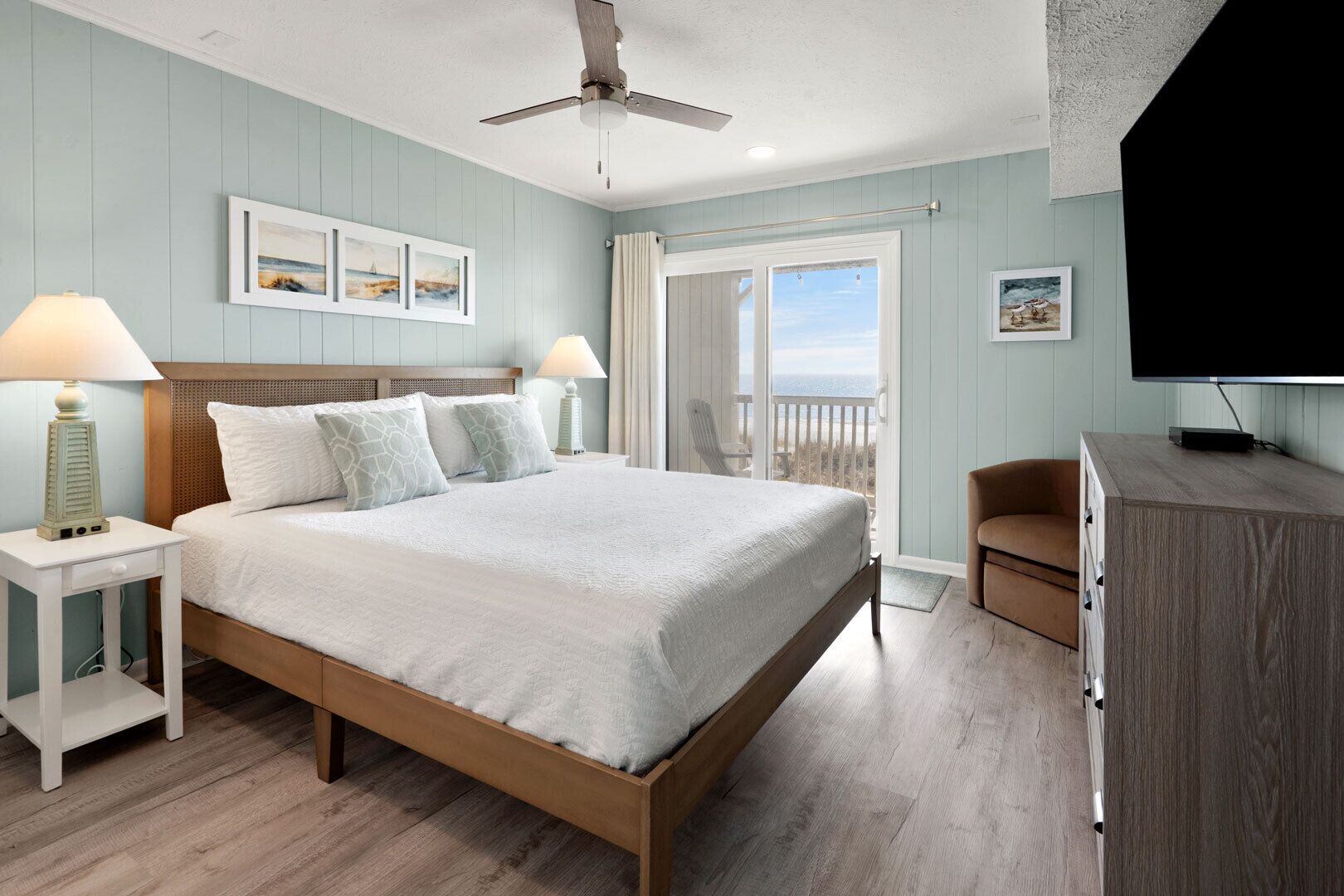 A bedroom with a bed, nightstands, a chair, a TV, and a balcony with a view.