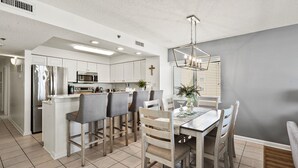 A modern kitchen with white cabinets, a stainless steel refrigerator, and a dining area with a wooden table and chairs.
