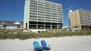 A beachfront hotel with multiple floors, outdoor seating, and a sandy beach in the foreground.