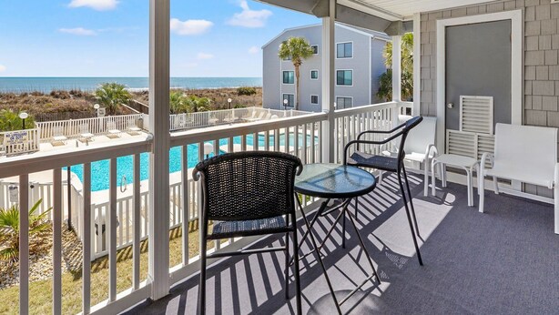 A balcony with a pool, white furniture, and a view of the ocean and buildings. - Oceanfront escape with pool & balcony views — peaceful 2BR retreat near Main Street & Cherry Grove (North Myrtle Beach)