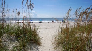 A sandy beach with people and umbrellas, leading to the ocean. - Oceanfront escape with pool & balcony views — peaceful 2BR retreat near Main Street & Cherry Grove (North Myrtle Beach)