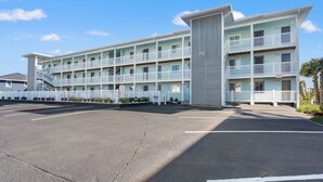 A multi-story motel with a central tower, outdoor parking, and a white fence.