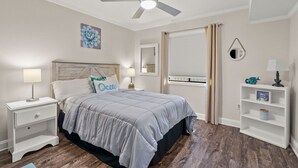 A bedroom with a bed, nightstands, a ceiling fan, a window with curtains, and a small shelf with decorative items.