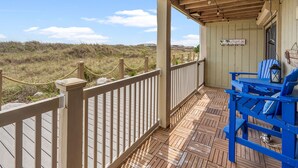 A wooden deck with a railing, a table with blue chairs, and a sign reading "Hawaiian by the Beach".