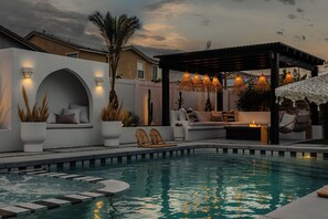 A pool area with a seating area, a pergola with hanging lights, and a fire feature. - Indah: Luxury Desert Oasis with Resort-Style Pool, Spa & Unforgettable Stays (Coachella)