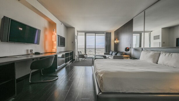 A modern hotel room with a large bed, a desk with a chair, a TV, and a view of the city. - SVS: Sunset View Studio | Open Balcony | Pool & Gym | Palms Place (Las Vegas)
