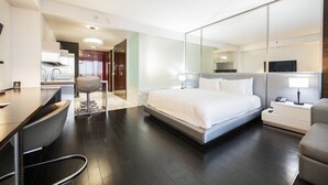 Habitación de hotel moderna con una cama grande, un escritorio y una silla. Hay un espejo en una pared y un televisor en otra.