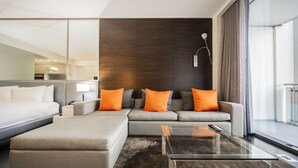 Una habitación de hotel moderna con una cama grande, un sofá, una mesa de centro de vidrio y vistas a la ciudad.