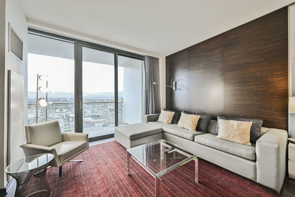 A modern living room with a sectional sofa, a glass coffee table, and a view of a cityscape through large windows.