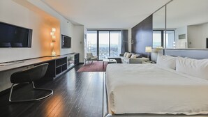 Moderni hotellihuone, jossa on suuri sänky, työpöytä tuolilla, televisio ja näkymä kaupunkiin.