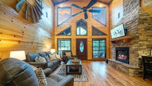 A cozy log cabin interior with a fireplace, wooden walls, and a ceiling fan. - Rustic Family Getaway 2BR - Hot Tub, Fire Pit, Pool Table, Pets OK (Broken Bow)
