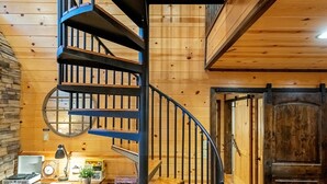 A spiral staircase in a wooden interior with a desk and books. - Rustic Family Getaway 2BR - Hot Tub, Fire Pit, Pool Table, Pets OK (Broken Bow)