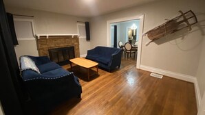 Ein Wohnzimmer mit Kamin, zwei blaue Sofas, einem Holztisch und einem Essbereich mit Tisch und Stühlen.