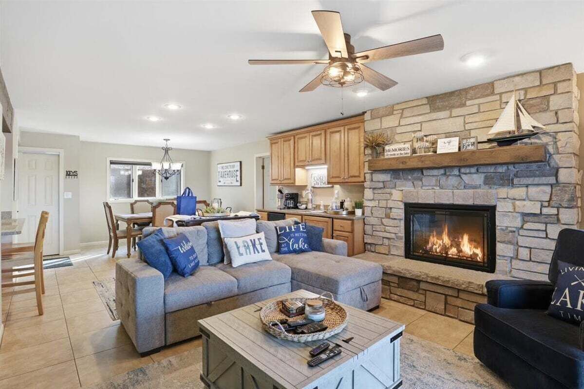 A living room with a stone fireplace, a ceiling fan, and a dining area in the background.