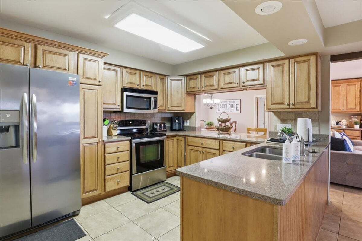 A kitchen with wooden cabinets, a stainless steel refrigerator, a microwave, an oven, a sink, and a breakfast bar.