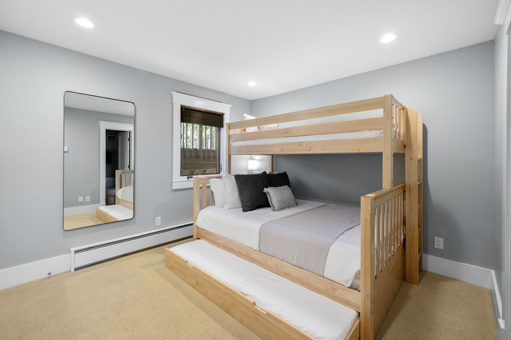 A bedroom with a bunk bed, a large mirror, a window with blinds, and a carpeted floor.