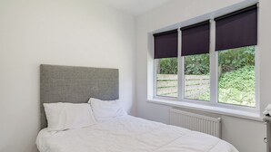 Une chambre à coucher avec un lit, un radiateur, une fenêtre avec des stores et une vue sur la verdure à l’extérieur.