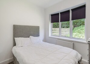 A bedroom with a bed, a radiator, a window with blinds, and a view of greenery outside.