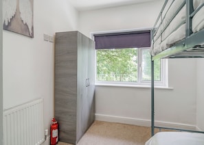 A room with bunk beds, a window with a view of trees, a radiator, and a fire extinguisher. - Beacon Fell Cottage 1 (Longridge, Ribble Valley)