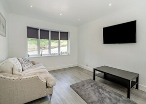 A modern living room with a sofa, a flat-screen TV, a small table, and a window with blinds.