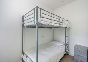 Ein Stockbett mit einer Matratze und Kissen, eine Kommode mit Schubladen sowie ein Lichtschalter an der Wand.