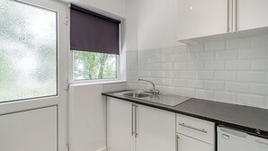 Une cuisine avec une fenêtre, des meubles blancs, un évier et un lave-vaisselle.