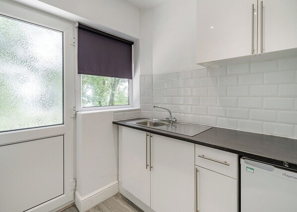 A kitchen with a window, white cabinets, a sink, and a dishwasher.