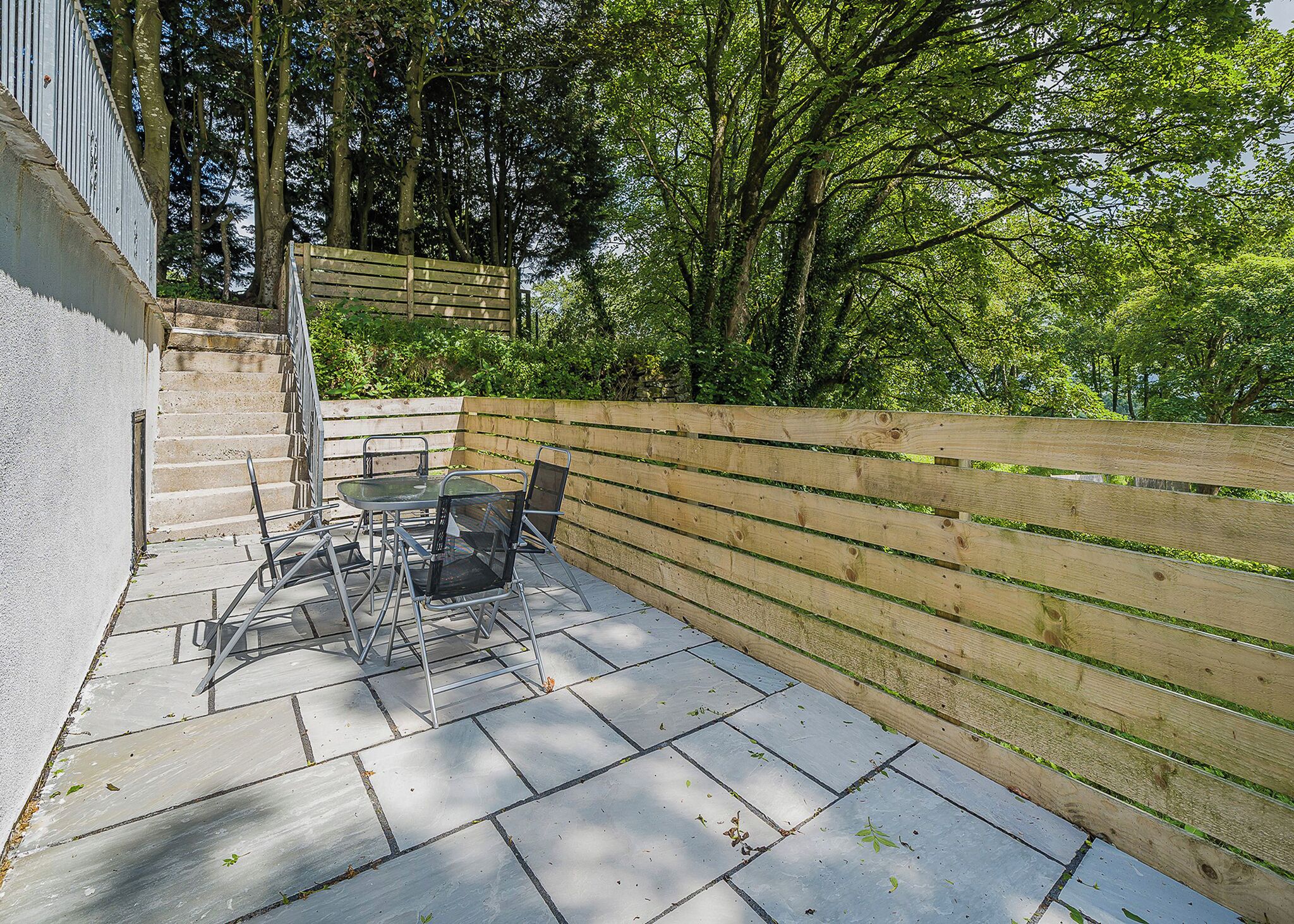 A patio with a table and chairs, a wooden fence, and a staircase leading to a higher level.