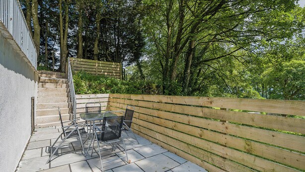 Une terrasse avec une table et des chaises, une clôture en bois et un escalier menant à un niveau supérieur.