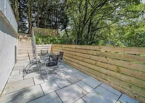A patio with a table and chairs, a wooden fence, and a staircase leading to a higher level. - Beacon Fell Cottage 1 (Longridge, Ribble Valley)