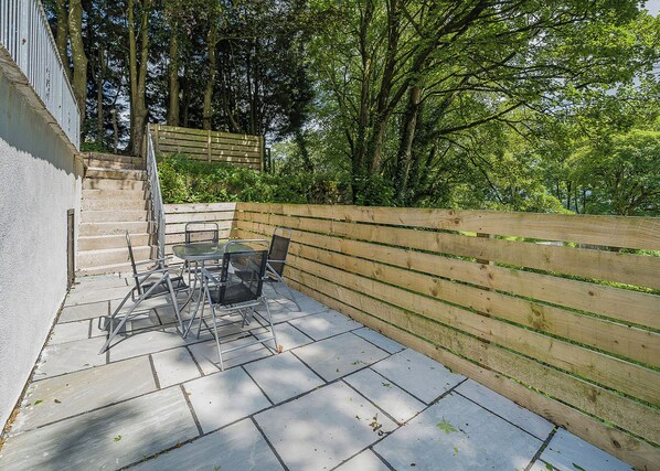 A patio with a table and chairs, a wooden fence, and a staircase leading to a higher level.