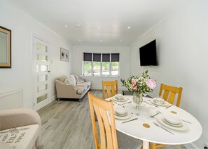 A dining area with a round table set for four, a sofa, and a TV mounted on the wall.