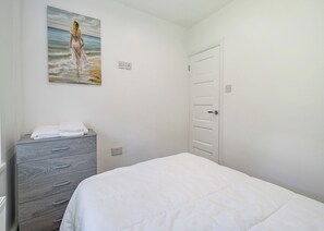 A bedroom with a bed, a dresser, a painting of a woman by the sea, and a door. - Beacon Fell Cottage 1 (Longridge, Ribble Valley)